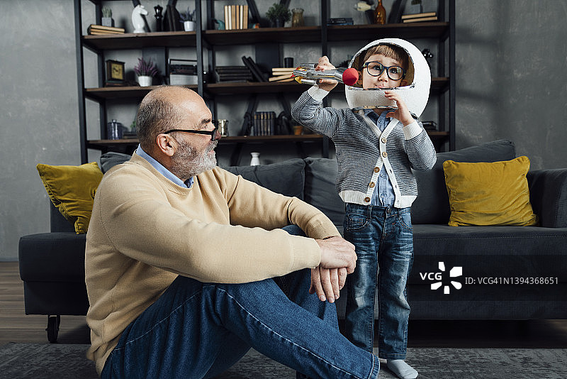 年长的男人看着戴着太空头盔玩玩具火箭的孙子图片素材