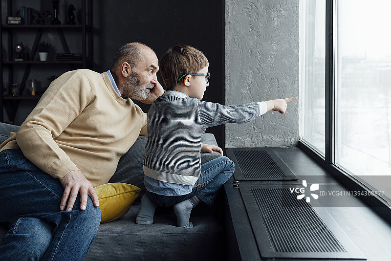 在家中，爷爷坐在沙发上，男孩指向窗外图片素材