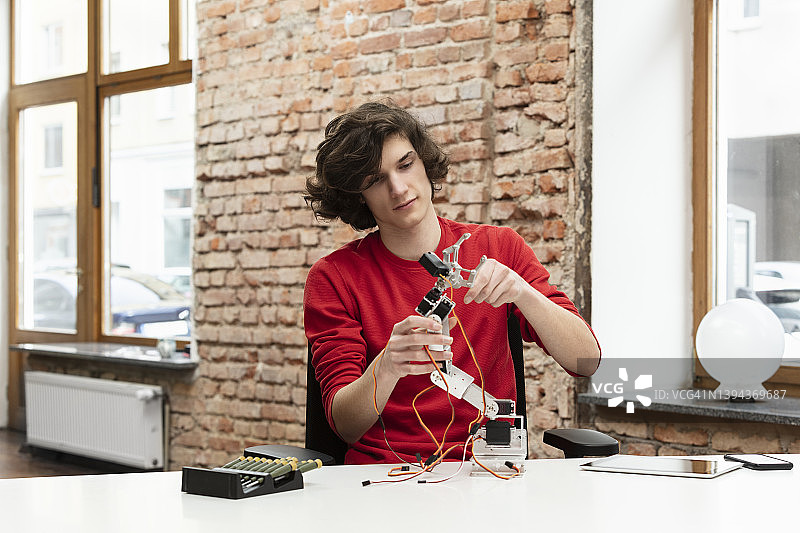 坐在桌旁研究机械臂的青少年男孩图片素材