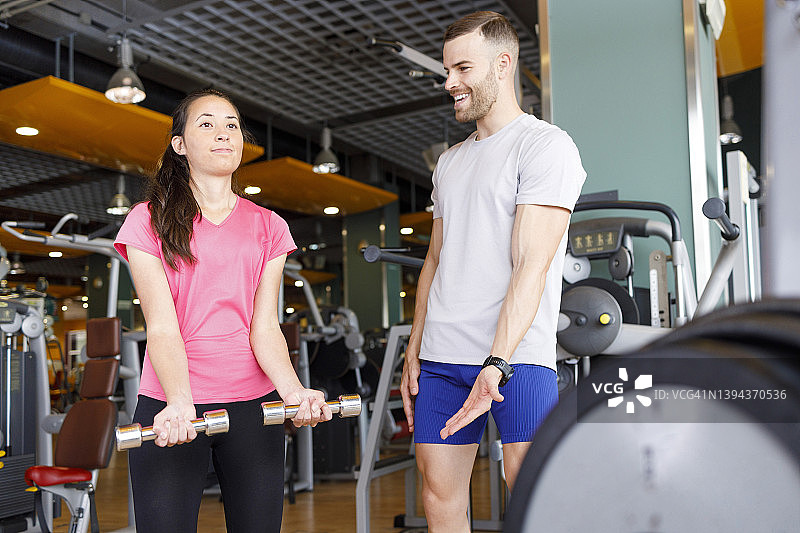 快乐的教练在健身房激励女性用哑铃锻炼图片素材