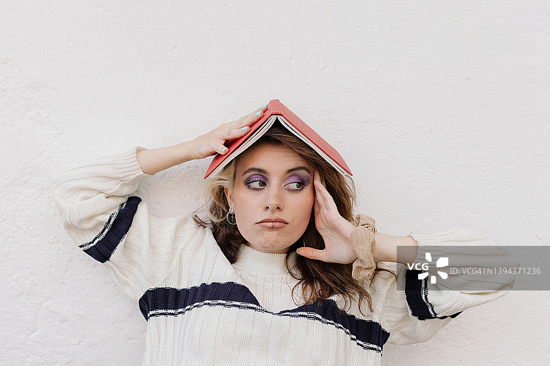 无聊的年轻女子在白墙前头顶着书图片素材