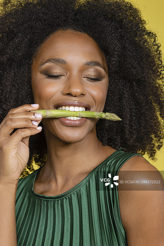 闭着眼睛咬芦笋的年轻女子，背景为黄色图片素材