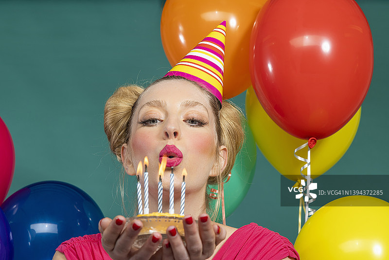 年轻女子戴着派对帽，在绿色背景下吹生日蛋糕上的蜡烛图片素材