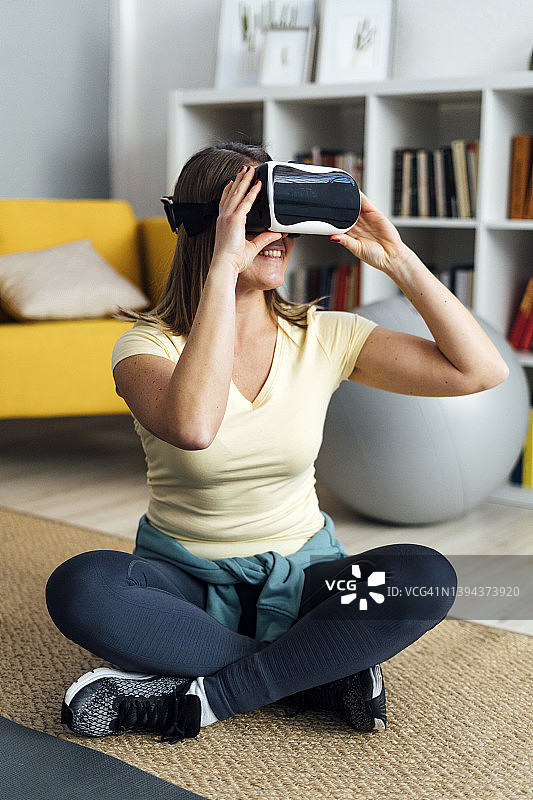 在客厅里盘腿坐着，戴着VR模拟器的微笑女人图片素材