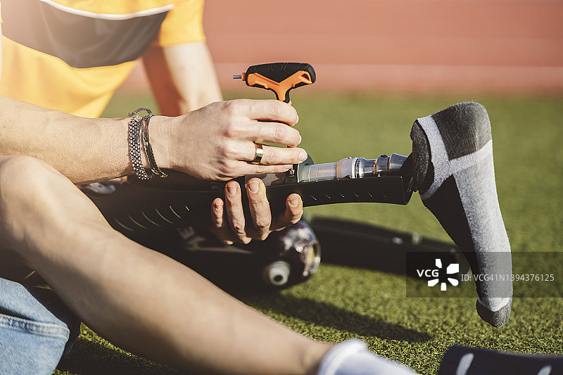 坐在草地上用螺丝刀调整假肢的残疾男子图片素材