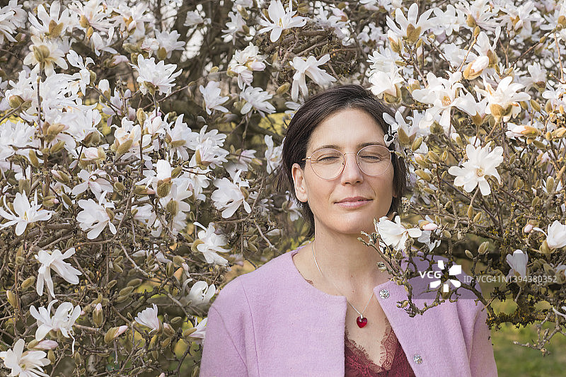 笑容满面的女人站在盛开的玉兰树旁图片素材