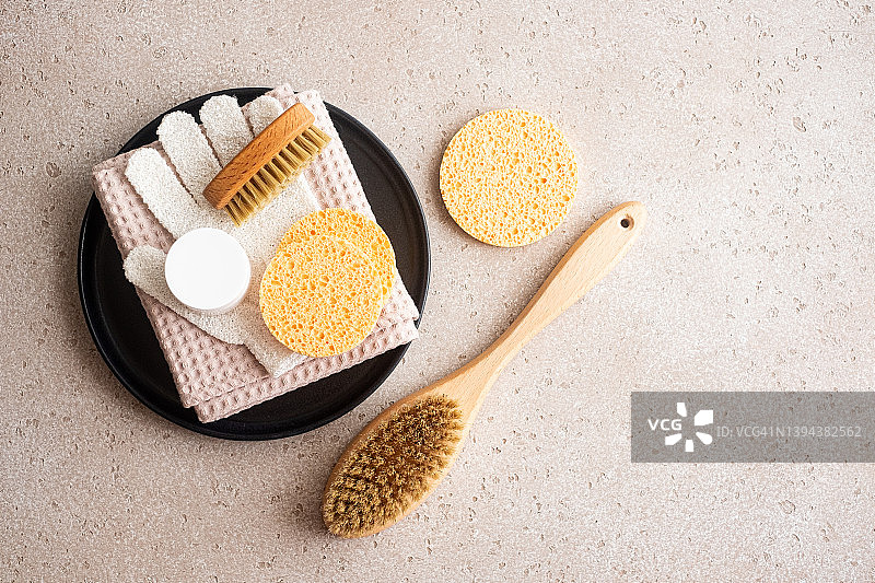 一套环保身体护理必需品（木制身体刷、清洁手套、清洁海绵、保湿霜）在水泥背景上。平铺。零浪费概念。饮食概念。图片素材