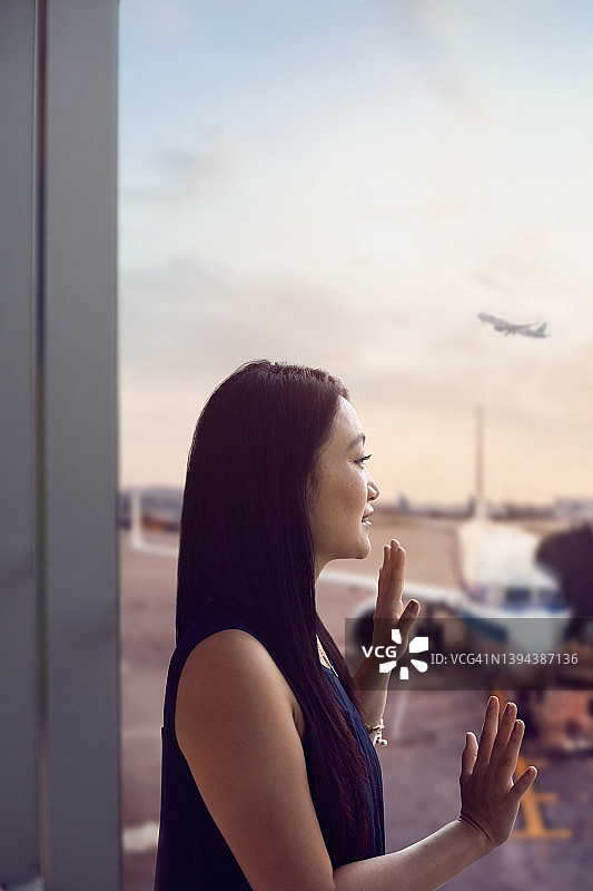 在机场航站楼向飞机挥手的年轻中国女人图片素材