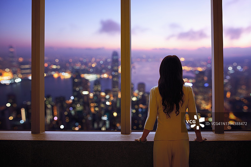 穿着西装的年轻女人在建筑物窗口眺望香港天际线图片素材