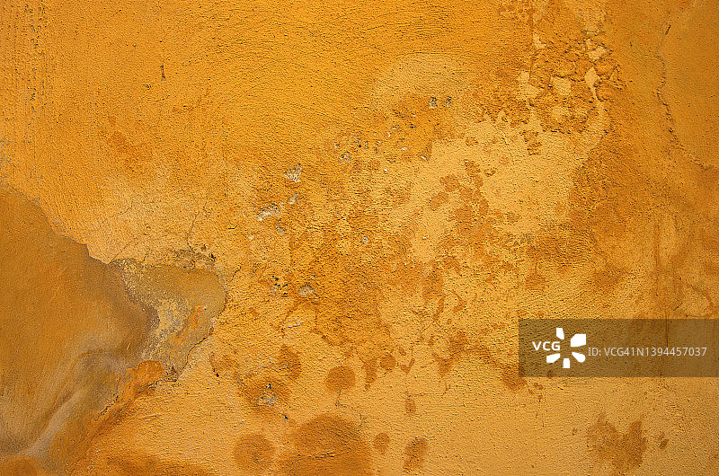褪色的、剥落的、潮湿的杂色灰泥墙，漆成橙黄色图片素材