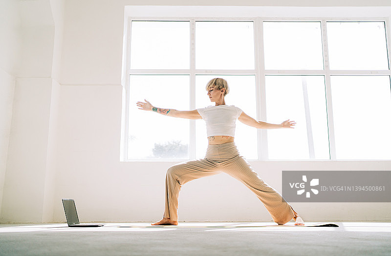 金发女子在窗前瑜伽垫上做战士姿势图片素材