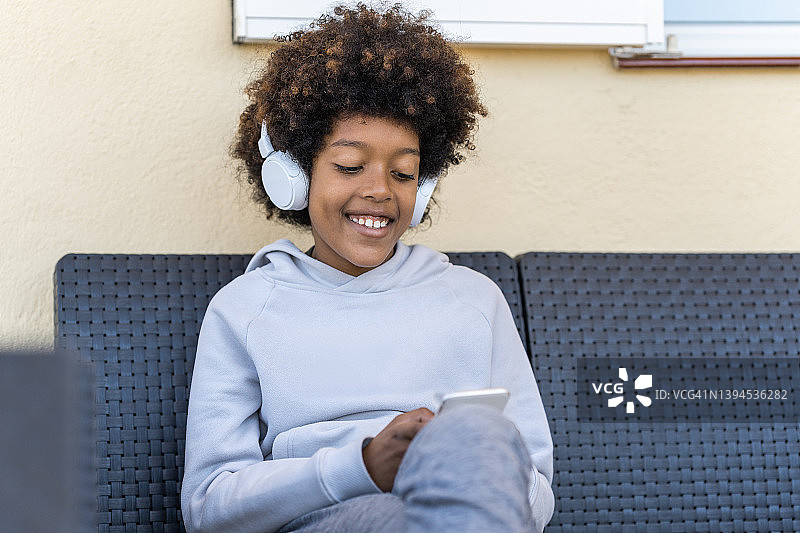 戴着耳机在沙发上用手机的微笑男孩图片素材