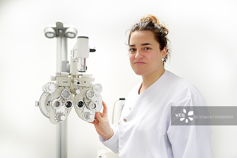 自信的棕发女性在验光师办公室使用光学折射仪，看着镜头，视力保健概念图片素材