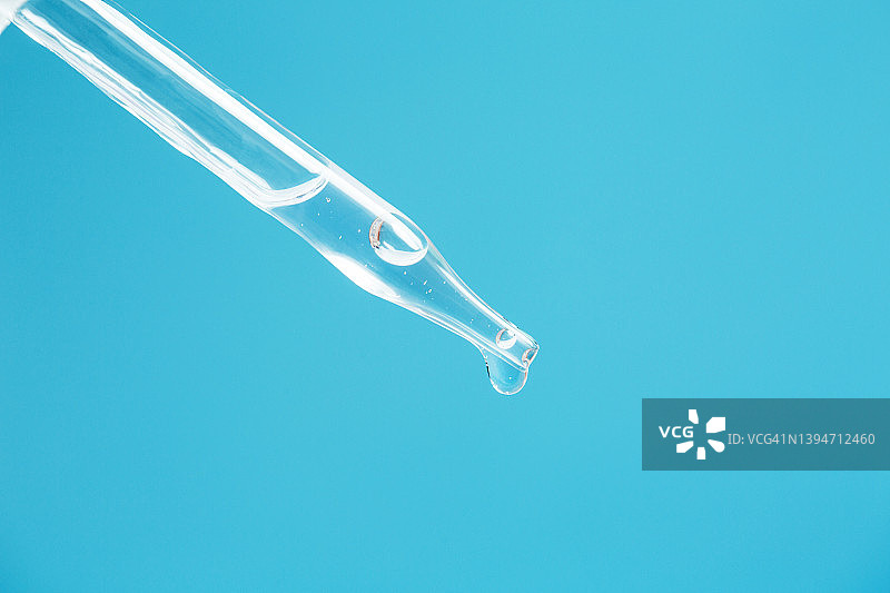 浅蓝色背景上，带有气泡的精华液滴从滴管滴落，正面特写图片素材