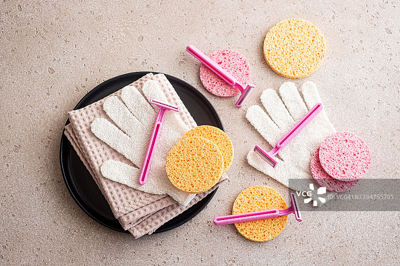 一套身体护理必需品（一次性剃须刀、清洁手套、清洁海绵、棉毛巾）在水泥背景上。居家水疗，平铺。剃须概念。图片素材