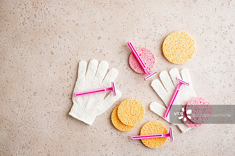一套身体护理必需品（一次性剃须刀、清洁手套、清洁海绵、棉毛巾）在水泥背景上。居家水疗，平铺。剃须概念。图片素材