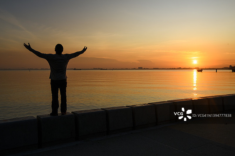 日出时，一个男人张开双臂，呈现剪影效果图片素材