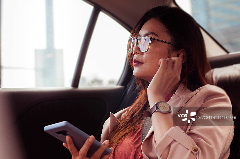 一位穿着时尚休闲的东南亚女子在汽车后座使用智能手机图片素材