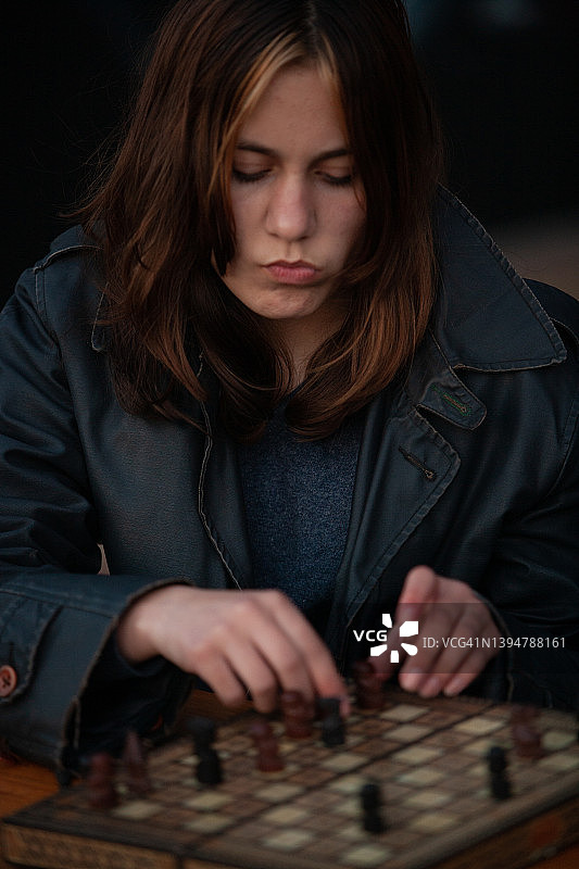 一位美丽的年轻少女正在思考她的下一步行动，在国际象棋或生活中，脸上带着若有所思的表情，双手试探性地移动图片素材