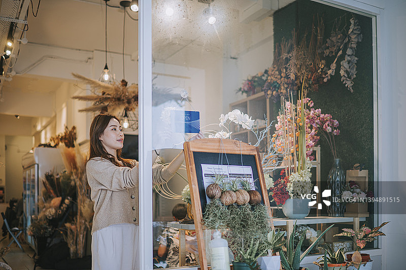 中国女花店主重新开业，在玻璃窗前挂出开业标志图片素材