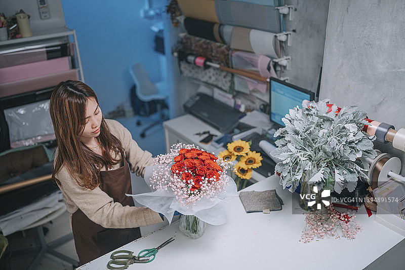 中国女性花艺师在花店柜台包装红色玫瑰花束图片素材