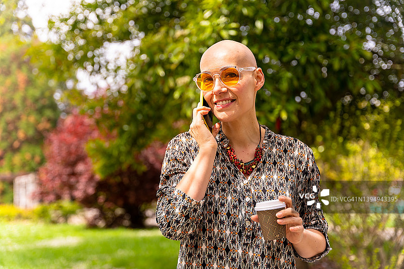 一位在乳腺癌后享受生活，戴着太阳镜在公园里树下打电话的中年白人妇女图片素材