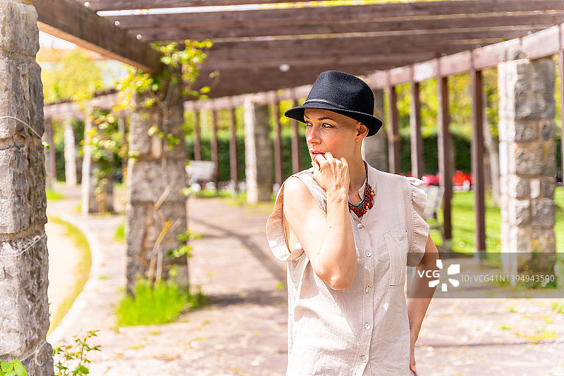 戴黑色帽子的高加索中年妇女在春天公园的拱门中散步，在公园里沉思，享受乳腺癌后的生活图片素材