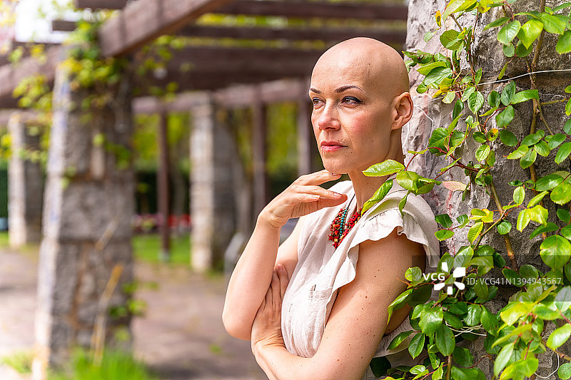 一位经历乳腺癌后在公园里享受生活的光头白人妇女的肖像，春天里笑着举起双臂图片素材