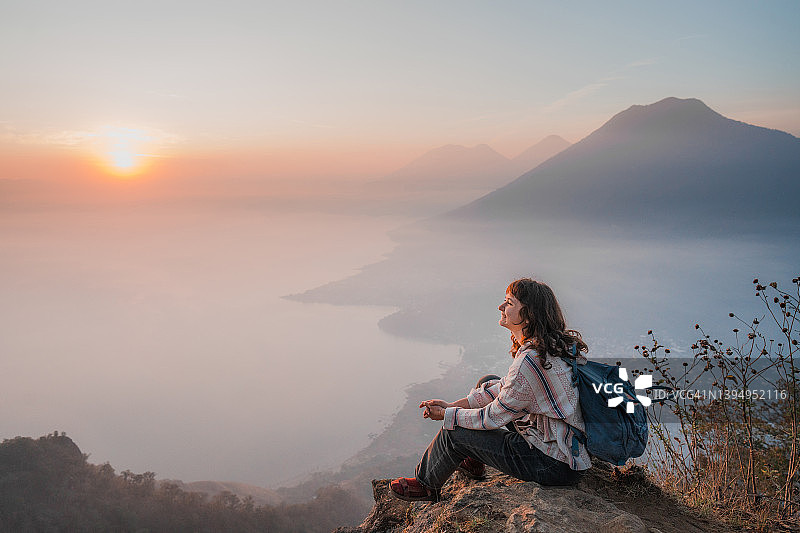 日落时分，女人坐在危地马拉阿蒂特兰湖背景的山上图片素材