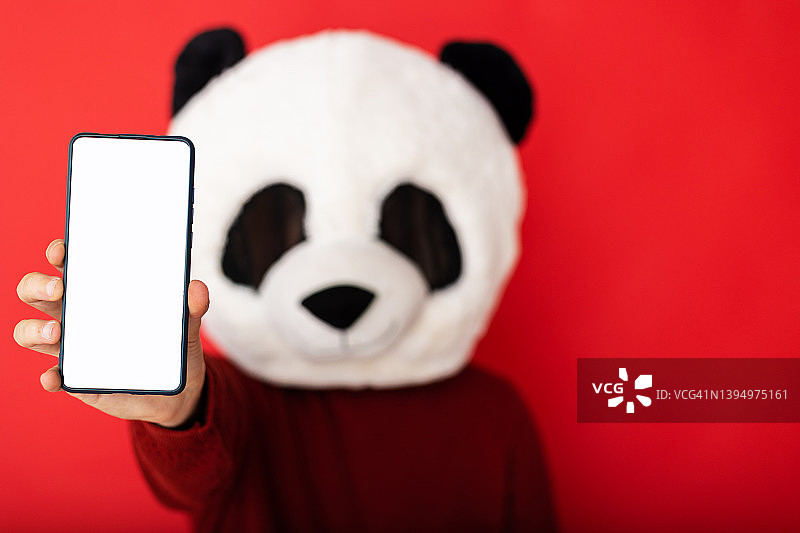 戴熊猫面具的男人展示红色背景上的手机白屏图片素材