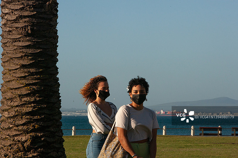 阳光明媚的蓝天下，两位年轻女子在开阔的田野上漫步图片素材