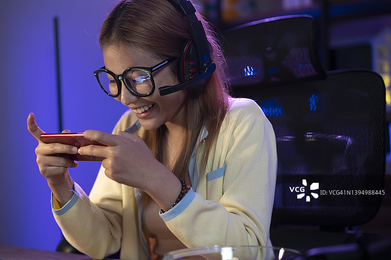 兴奋的亚洲女人晚上在家用智能手机玩手机游戏。图片素材