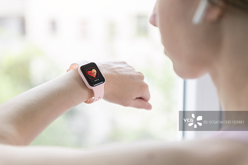 在家训练时，女人在粉色智能手表上查看心率图片素材