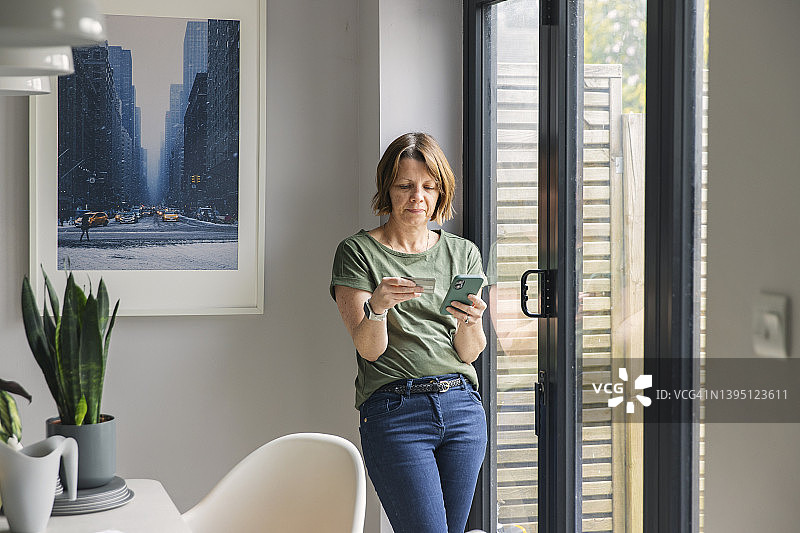 中年妇女在家使用信用卡和智能手机进行网上购物图片素材