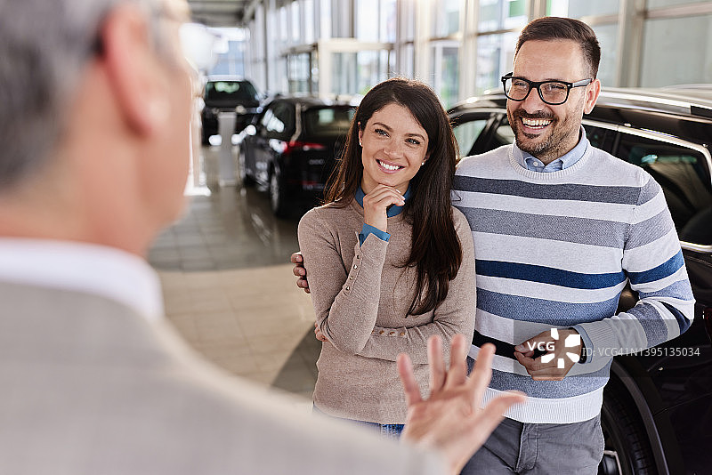 在展厅与汽车销售交谈的幸福夫妇图片素材