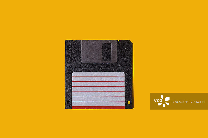 黄色背景上的黑色复古3.5英寸软盘，带白色和红色标签，计算、计算机、存储、复古、磁盘和数据存储概念图片素材