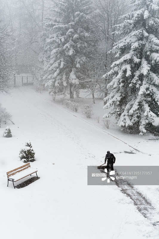 城市公园冬天下雪。人的剪影从雪中清理道路。图片素材