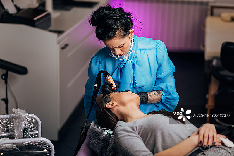 专注的美容师为千禧一代女性纹眉图片素材