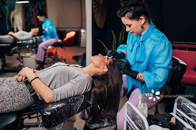 戴着黑色手套的美容师在纹身椅上为安静躺着的女人纹眉图片素材