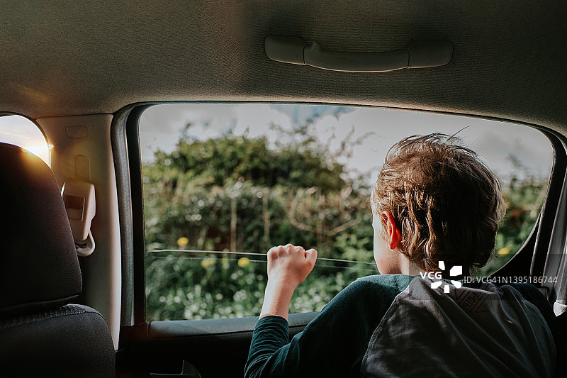 阳光明媚的日子里，坐在汽车后座的小男孩望着窗外图片素材