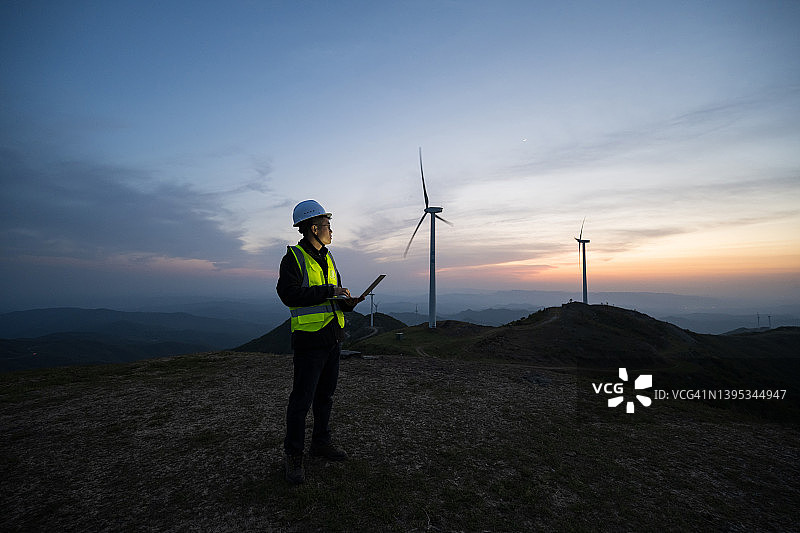 傍晚，亚洲男电气工程师手提电脑站在风力发电厂图片素材