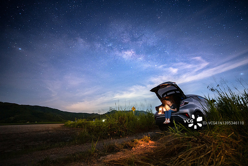 年轻美女坐在SUV汽车后，在周末银河星空下看书放松图片素材