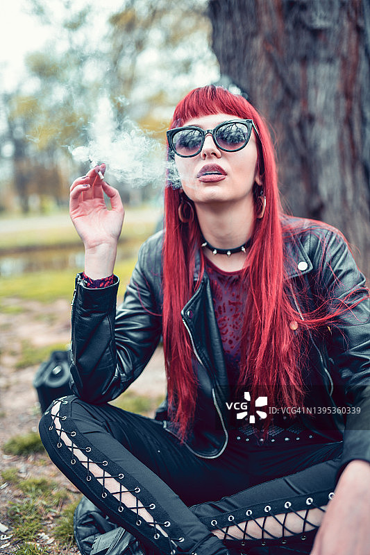 美丽的哥特式红发女子在公园吸烟图片素材