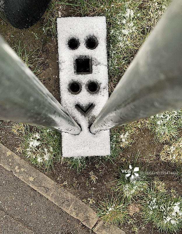 混凝土块上的笑脸和尖叫人脸的幻想，用于固定路边建筑工地的金属围栏柱，并覆盖着小雪。图片素材