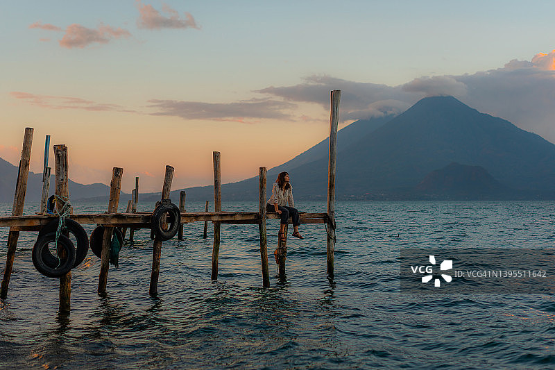 日落时分，坐在危地马拉阿蒂特兰湖码头上的女人图片素材