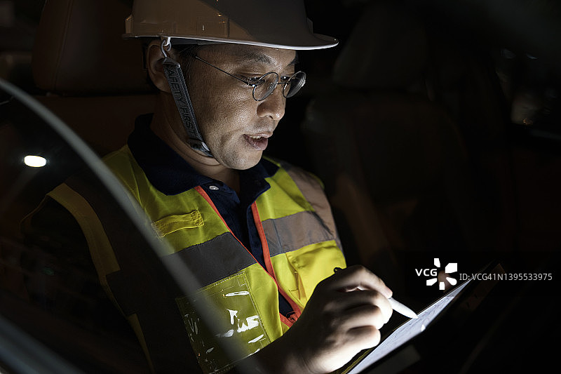 现场服务和支持工程师解决方案。一名日本年长男性土木工程师或测量员工程师在现场调查期间在车内的平板电脑上做日常报告。图片素材