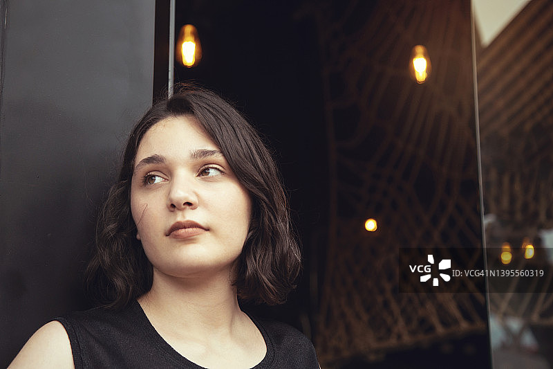 在黑色咖啡馆背景前摆姿势的迷人青年女子肖像图片素材