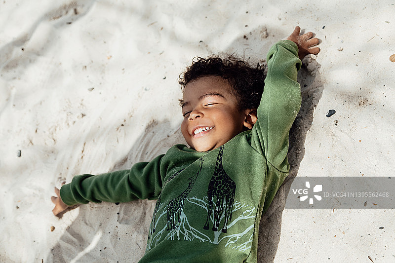 深色皮肤的非洲发型男孩躺在沙滩上微笑图片素材