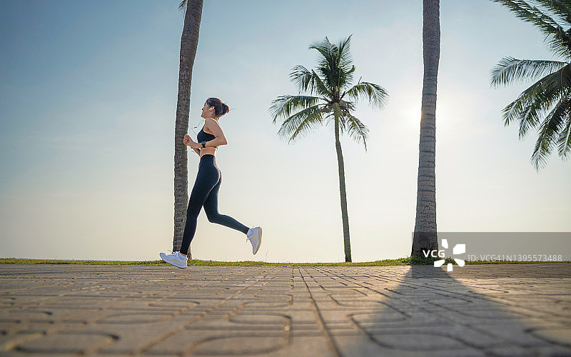 年轻的健身运动女性在公园跑步，戴着耳机在户外晨跑图片素材