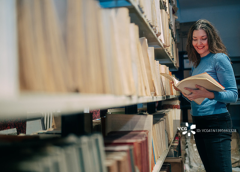 美丽的大学生站在图书馆的书架旁读书图片素材
